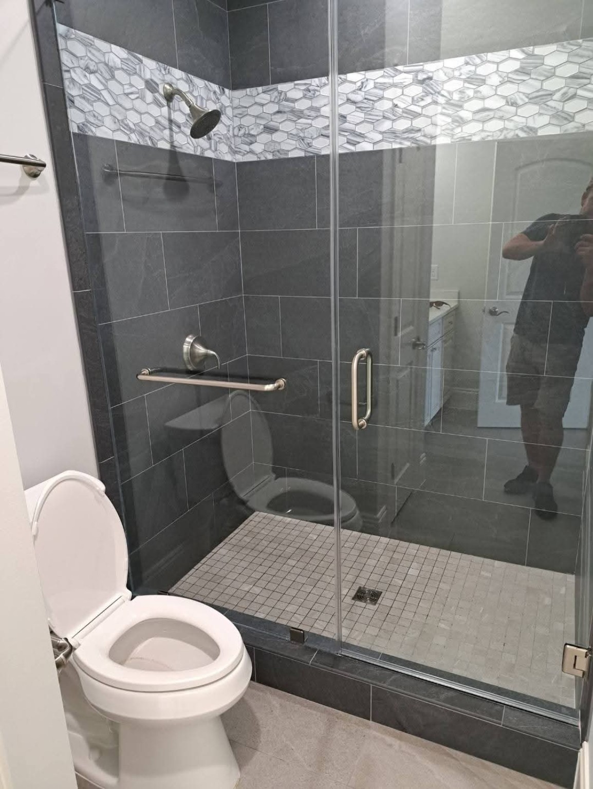 Walk-in shower with dark tile, glass enclosure and stainless fixtures